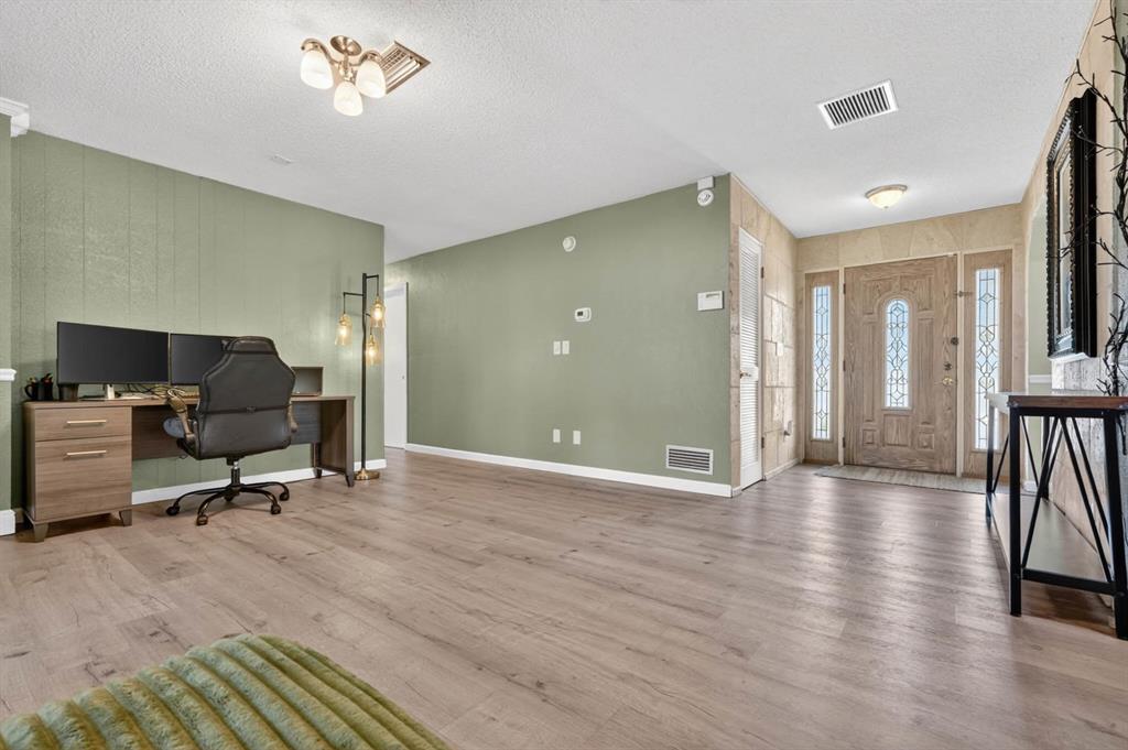 A room with sage green walls, wood-look flooring, a desk setup, and a wooden front door — 772 N BEACH STREET, ORMOND BEACH, FL