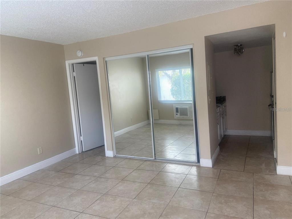 A room with beige walls, tiled floors, a mirrored closet, and an adjacent kitchen area — 4133 DOLPHIN DRIVE UNIT 4133, TAMPA, FL