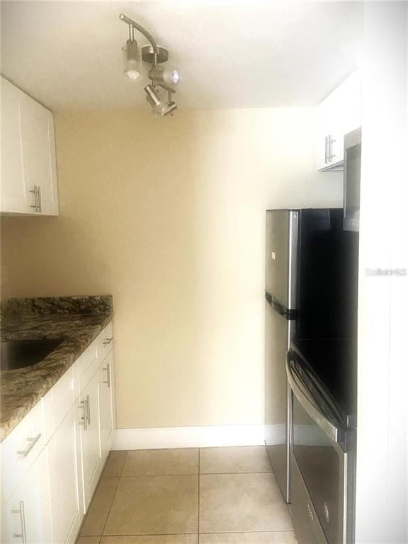 A small kitchen features white cabinets, granite countertops, and a stainless steel refrigerator — 4133 DOLPHIN DRIVE UNIT 4133, TAMPA, FL