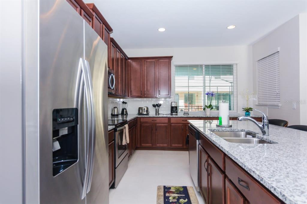 A kitchen features dark wood cabinets, granite countertops, stainless steel appliances, and a center island — 1534 CAREY PALM CIRCLE, KISSIMMEE, FL