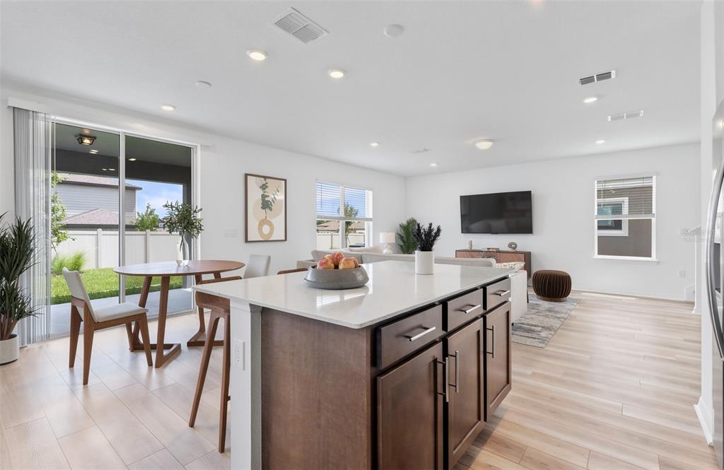 An open-concept kitchen and living area features a central island, wood-look flooring, and sliding doors — 1452 HAMILTON WAY, LAKE ALFRED, FL