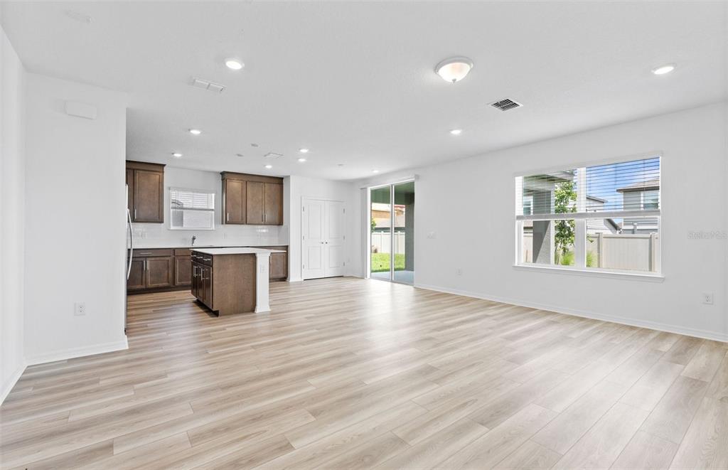 An open-concept kitchen and living area featuring wood-look flooring, white walls, and sliding glass doors — 1452 HAMILTON WAY, LAKE ALFRED, FL