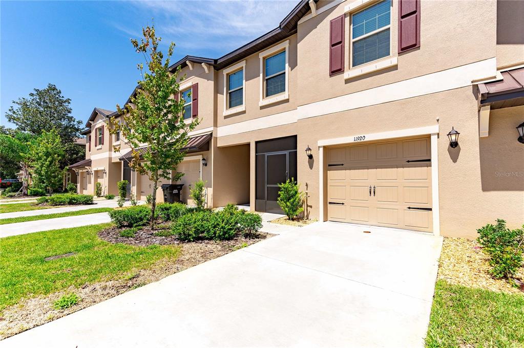 A tan two-story townhouse features a single-car garage, a screened entryway, and a concrete driveway — 11920 CASTINE STREET, NEW PORT RICHEY, FL
