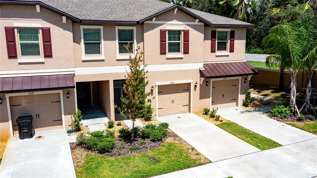 An exterior view of a multi-unit townhouse complex with tan stucco walls and brown shutters — 11920 CASTINE STREET, NEW PORT RICHEY, FL
