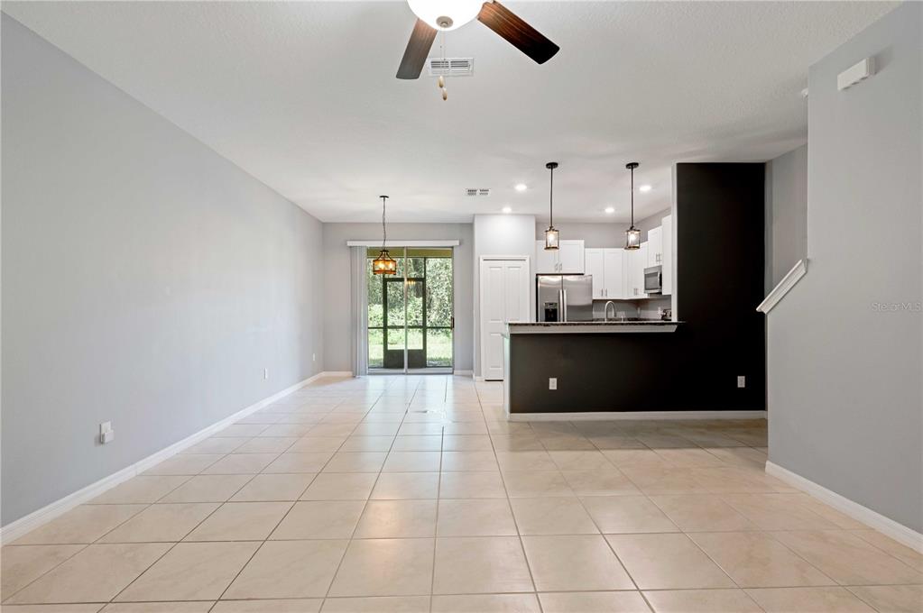 An open-concept living and dining area features light tile flooring, gray walls, and a kitchen — 11920 CASTINE STREET, NEW PORT RICHEY, FL