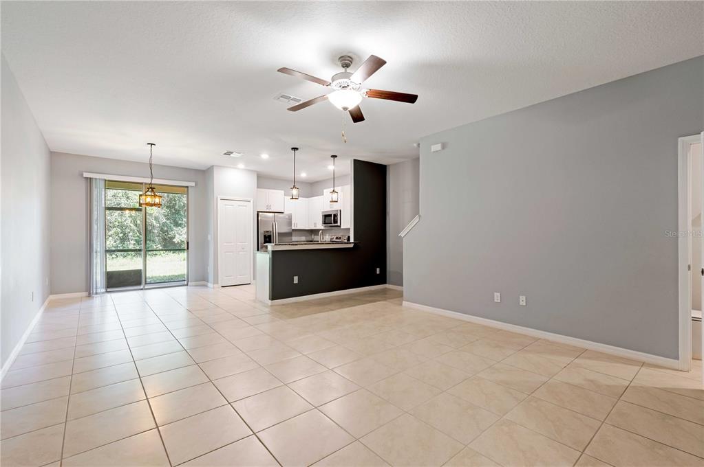An open-concept living and dining area features light tile flooring, gray walls, and a kitchen — 11920 CASTINE STREET, NEW PORT RICHEY, FL