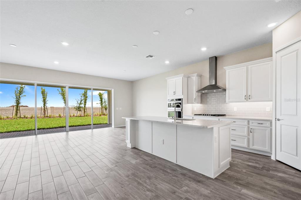 A modern kitchen with white cabinets, a large island, and sliding glass doors to a yard — 13348 PANAMA BEACH COURT, ORLANDO, FL