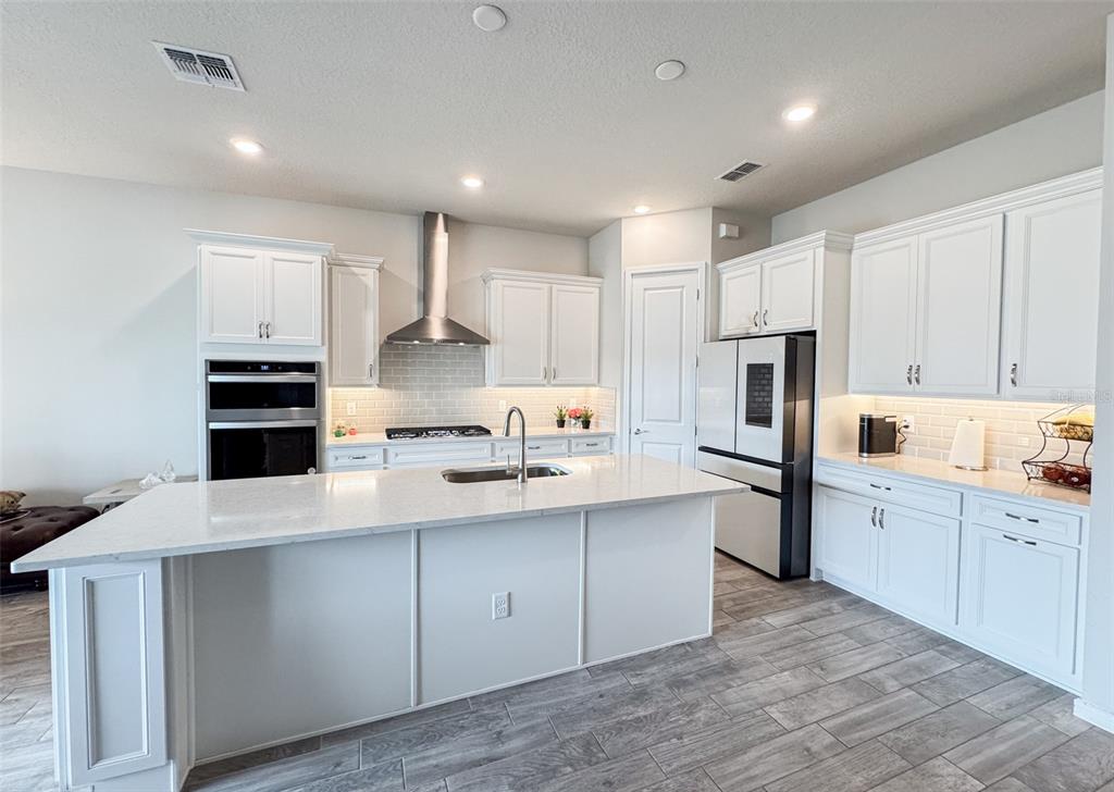 A modern kitchen features white cabinets, stainless steel appliances, a large island, and tile flooring — 13348 PANAMA BEACH COURT, ORLANDO, FL