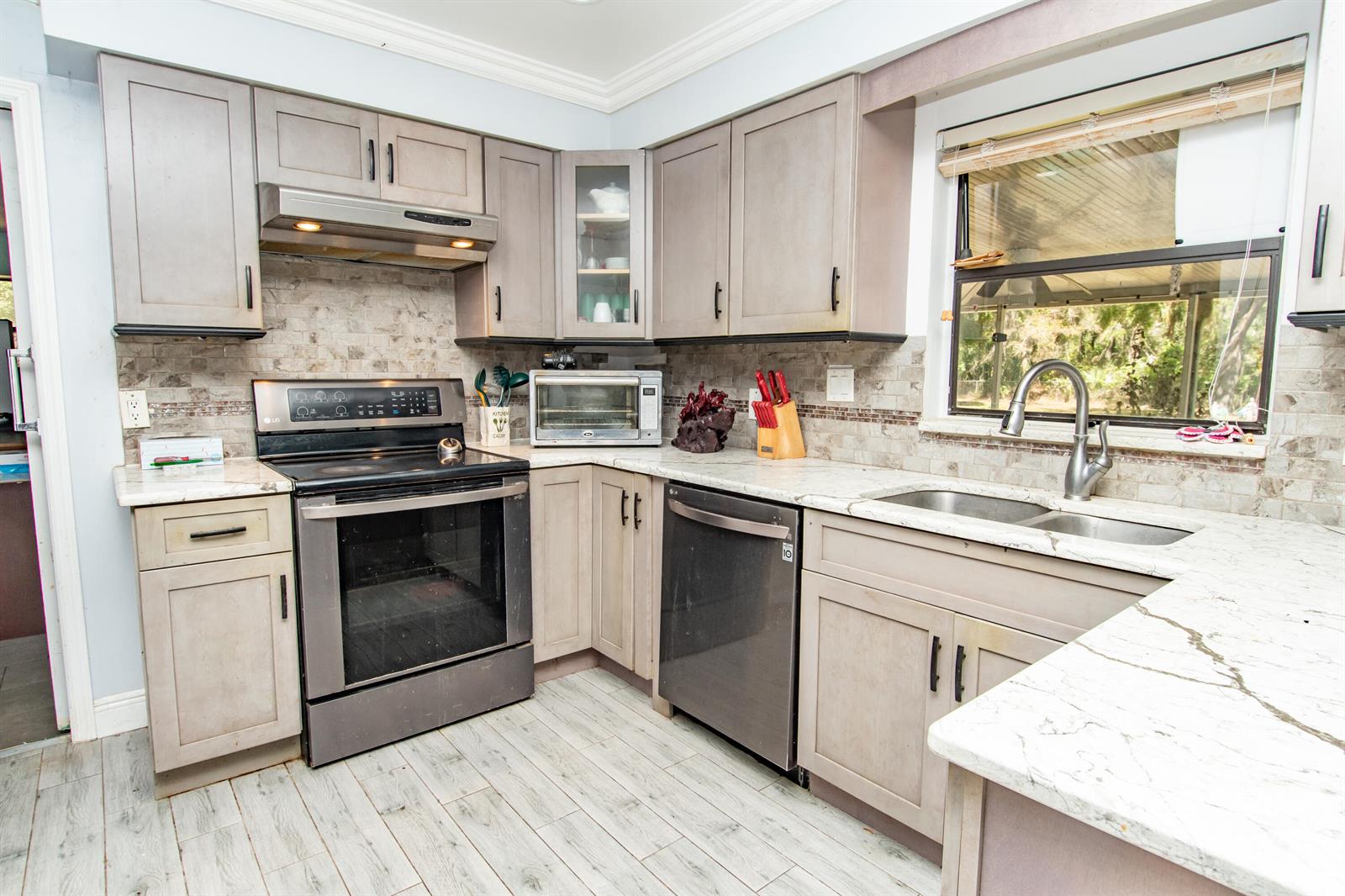 A kitchen features gray cabinets, stainless steel appliances, a tiled backsplash, and white marble countertops — 4022 Canaveral Groves Boulevard, Cocoa FL 32926, COCOA, FL