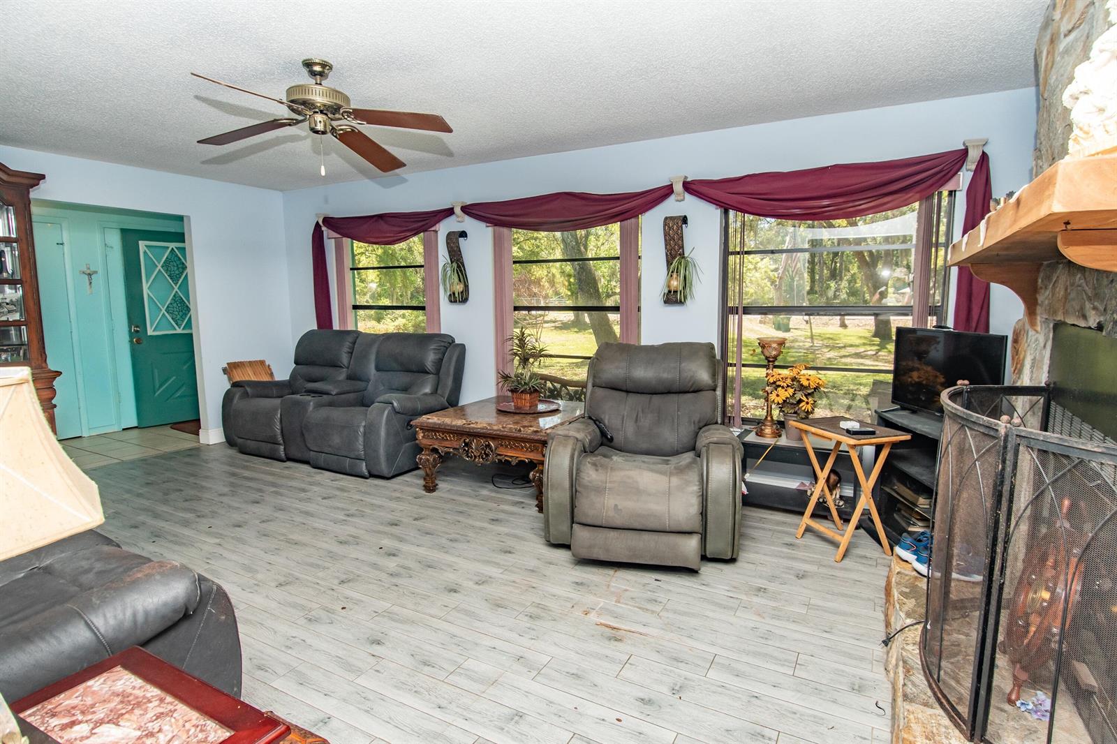 A living room features gray wood-look flooring, a stone fireplace, and three large windows — 4022 Canaveral Groves Boulevard, Cocoa FL 32926, COCOA, FL
