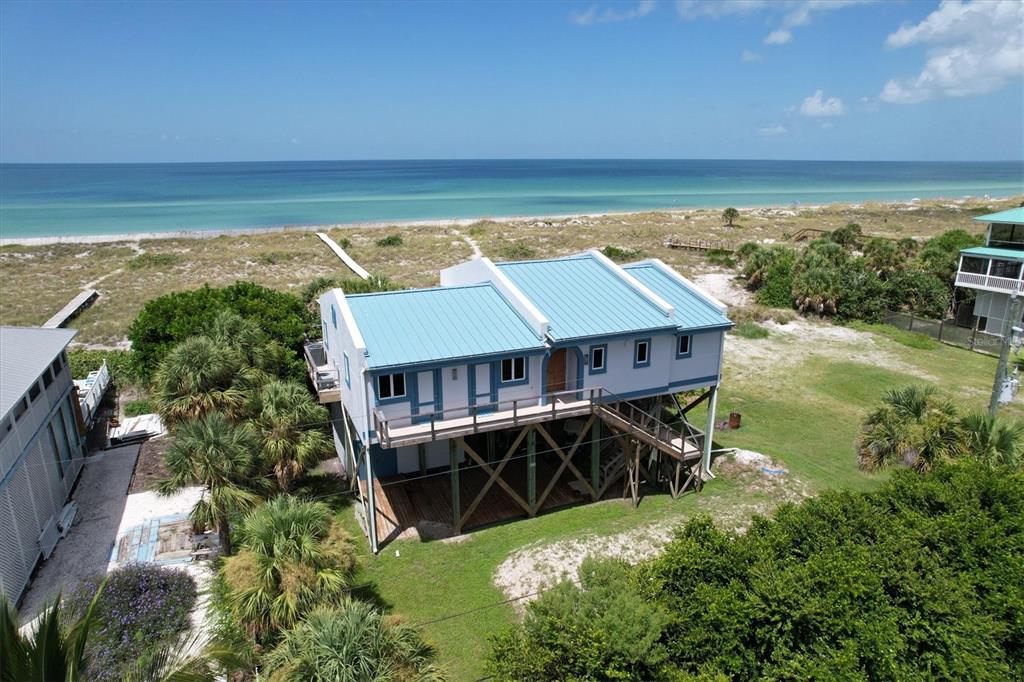 An elevated coastal house with a blue metal roof sits near a sandy beach — 9736 LITTLE GASPARILLA ISLAND UNIT B, PLACIDA, FL
