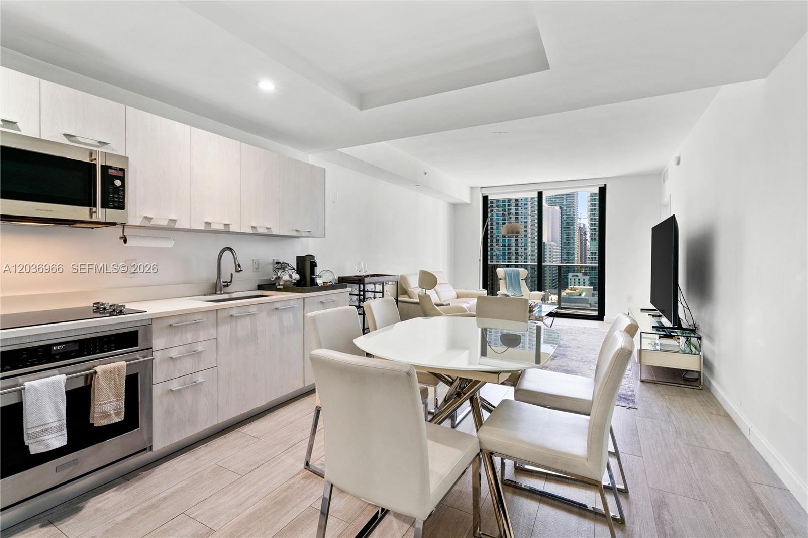 A modern apartment features a kitchen with light wood cabinets, a glass dining table, and floor-to-ceiling windows — 55 SW 9th St # 1904, Miami FL 33130, MIAMI, FL
