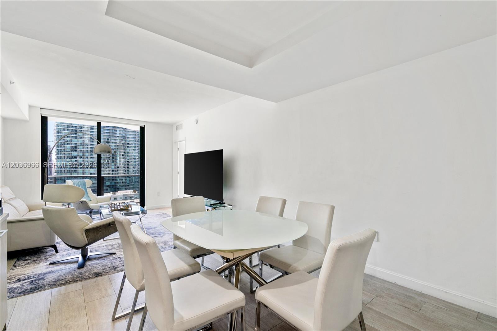 A dining area with a glass table and white chairs sits next to a living room — 55 SW 9th St # 1904, Miami FL 33130, MIAMI, FL