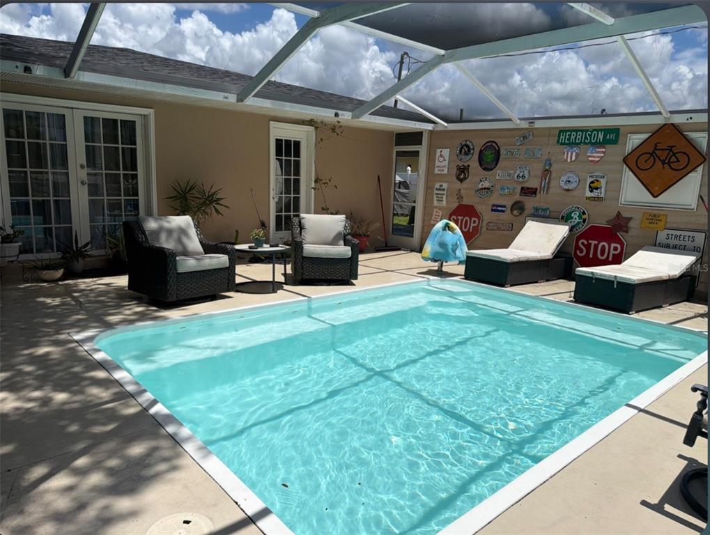 A screened-in patio features a rectangular swimming pool, wicker furniture, and potted plants — 8093 HERBISON AVENUE, NORTH PORT, FL