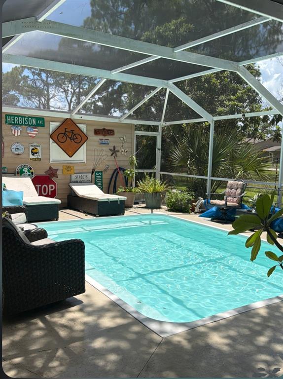 A backyard view featuring a screened-in pool enclosure, a detached garage, and mature trees — 8093 HERBISON AVENUE, NORTH PORT, FL