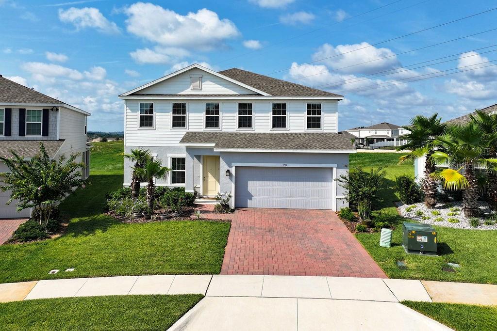 A two-story suburban house with a brick driveway, a two-car garage, and palm trees — 1193 WHISPERING LANE, MINNEOLA, FL
