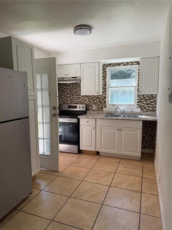 A kitchen features white cabinets, stainless steel appliances, a tiled backsplash, and tan floor tiles — 5976 SE 115TH STREET, BELLEVIEW, FL