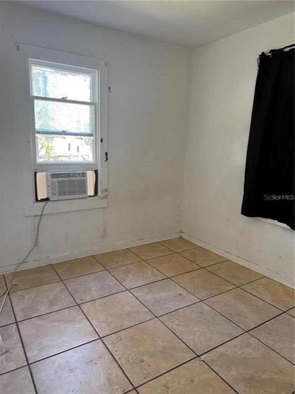 A room with light-colored tile flooring, white walls, a window air conditioner, and black curtains — 5976 SE 115TH STREET, BELLEVIEW, FL