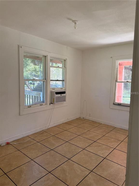 An empty room features white walls, tan tile flooring, two windows, and a window air conditioner — 5976 SE 115TH STREET, BELLEVIEW, FL
