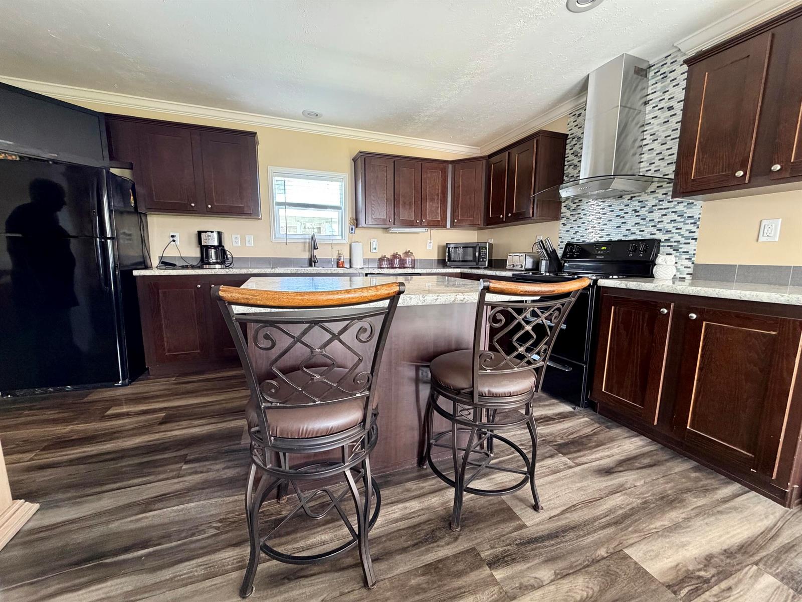 A kitchen features dark wood cabinets, a central island with two chairs, and stainless appliances — 106 Sandhill Boulevard, Fort Pierce FL 34982, FORT PIERCE, FL