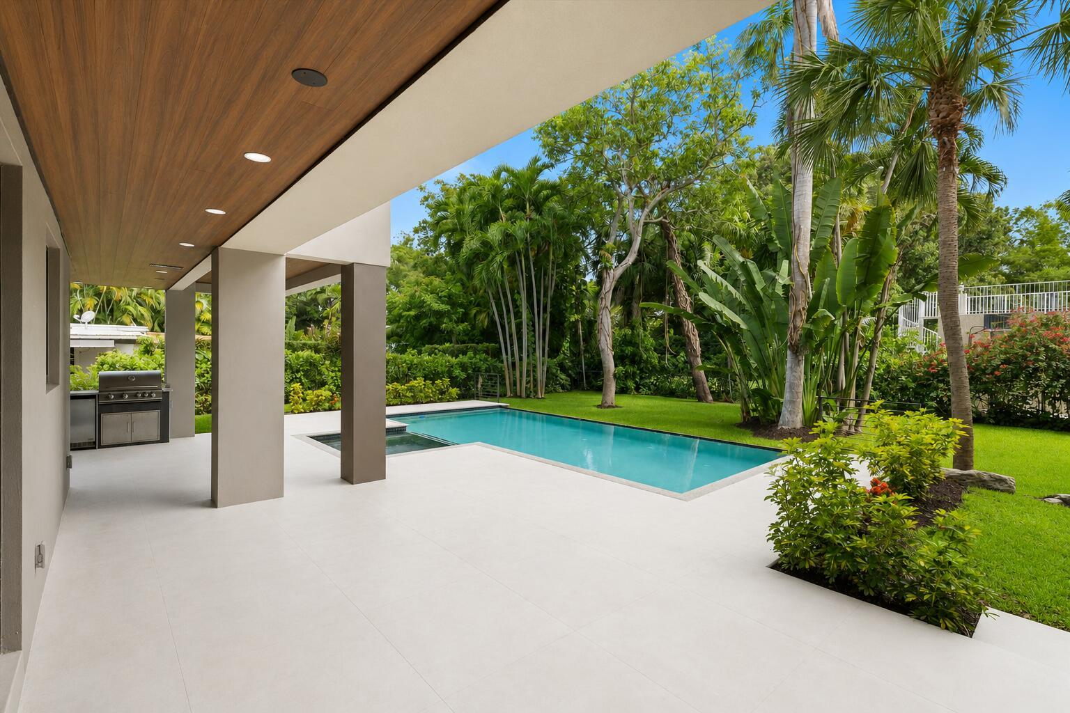A covered patio with a built-in grill overlooks a swimming pool and lush backyard — 451 NE 119th Street, Biscayne Park FL 33161, BISCAYNE PARK, FL