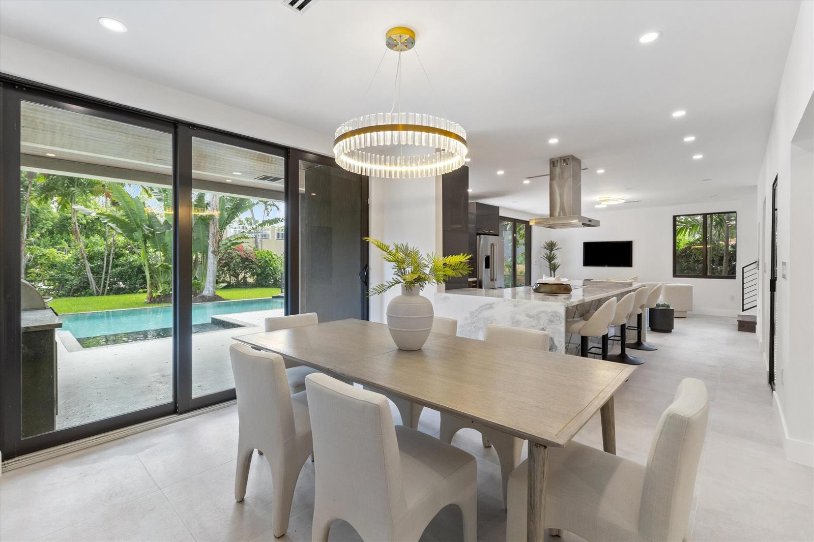 A dining area with a modern chandelier overlooks a backyard pool through large sliding doors — 451 NE 119th Street, Biscayne Park FL 33161, BISCAYNE PARK, FL