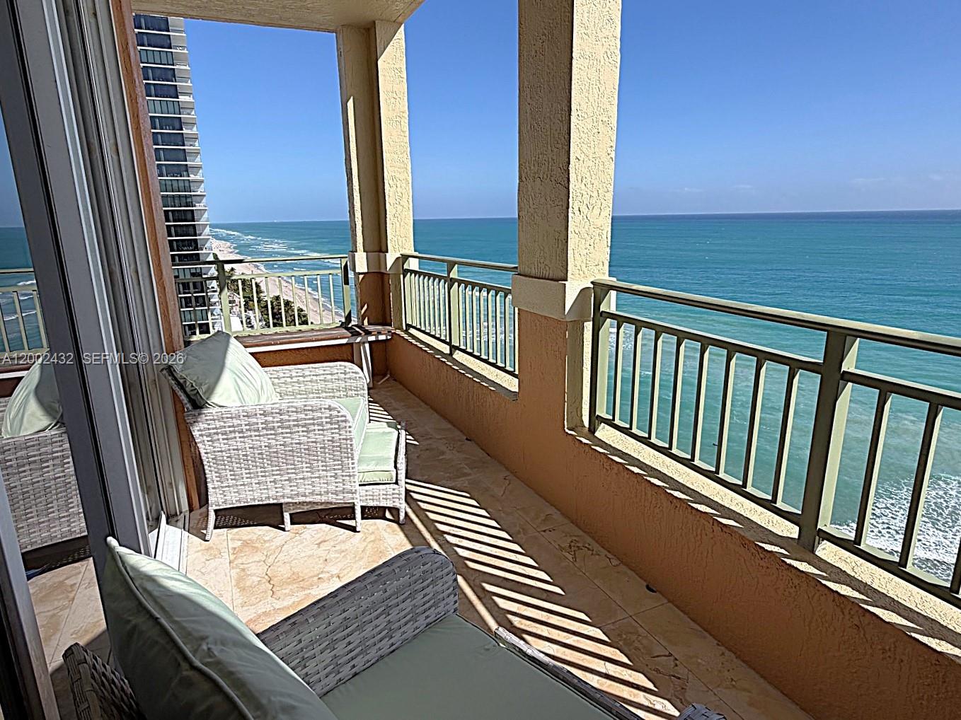 A balcony with wicker chairs overlooks the ocean and a neighboring high-rise building — 2080 S Ocean Dr, Hallandale Beach FL 33009, HALLANDALE BEACH, FL
