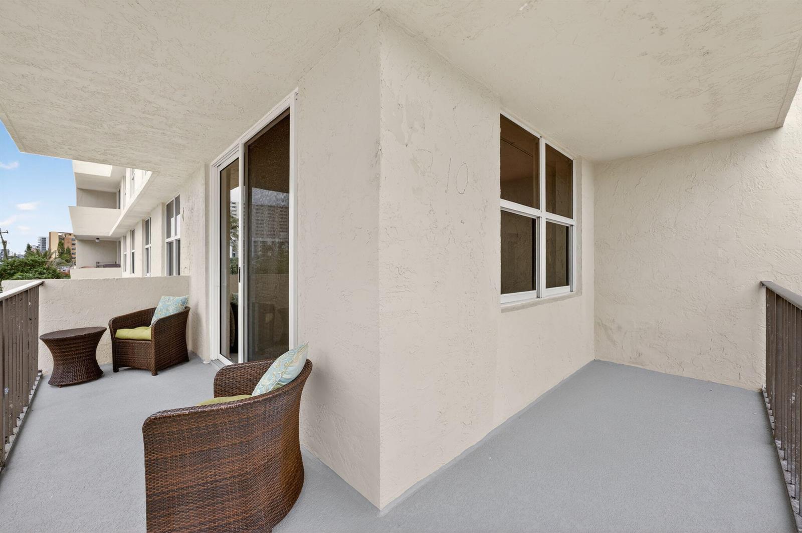 A balcony features wicker chairs, a small table, sliding glass doors, and concrete flooring — 1009 N Ocean Boulevard # 312, Pompano Beach FL 33062, POMPANO BEACH, FL
