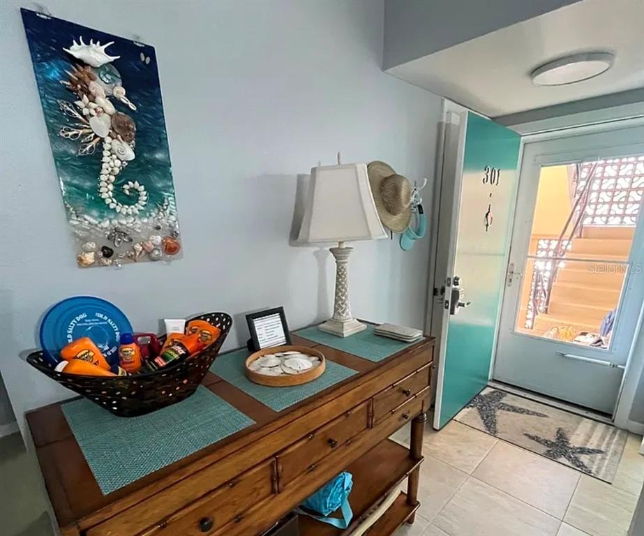 An entryway features a wooden console table, coastal decor, and a door leading to stairs — 1250 N PORTOFINO DRIVE UNIT 301, SARASOTA, FL
