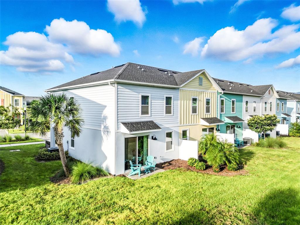 A multi-unit residential building with white, yellow, and teal siding and a grassy backyard — 3184 CARIBBEAN SOUL DRIVE, KISSIMMEE, FL