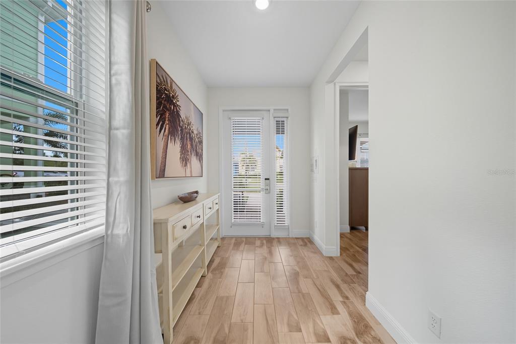 A bright entryway features light wood-look tile flooring, a console table, and a glass-paneled door — 3184 CARIBBEAN SOUL DRIVE, KISSIMMEE, FL