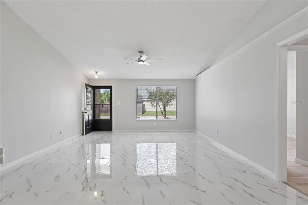 A bright living room features white marble-look tile flooring, a vaulted ceiling, and a black door — 5588 GARDEN GROVE CIRCLE, WINTER PARK, FL