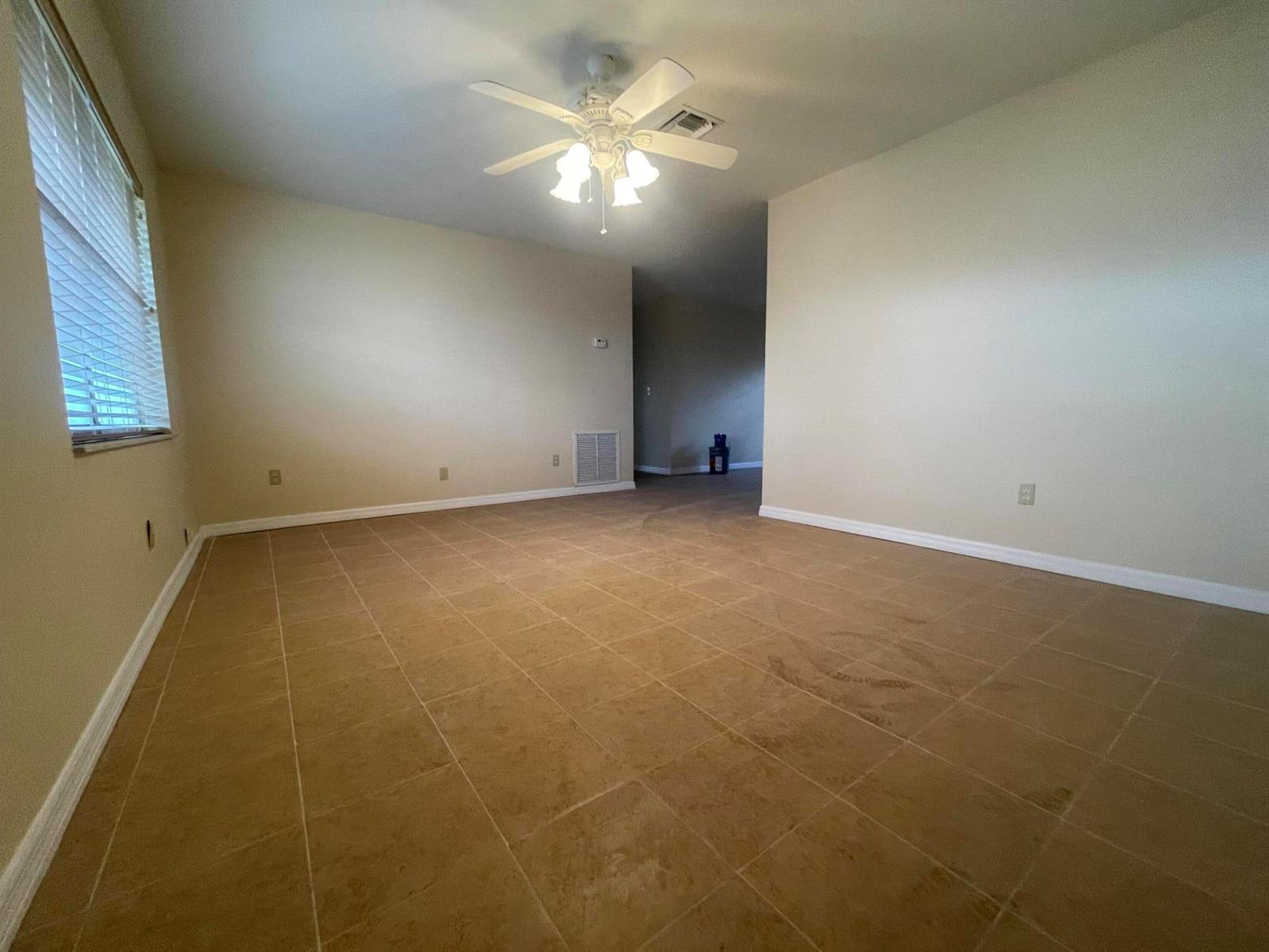 An empty room with tan tile flooring, beige walls, a ceiling fan, and a window — 3101 Avenue T, Fort Pierce FL 34947, FORT PIERCE, FL