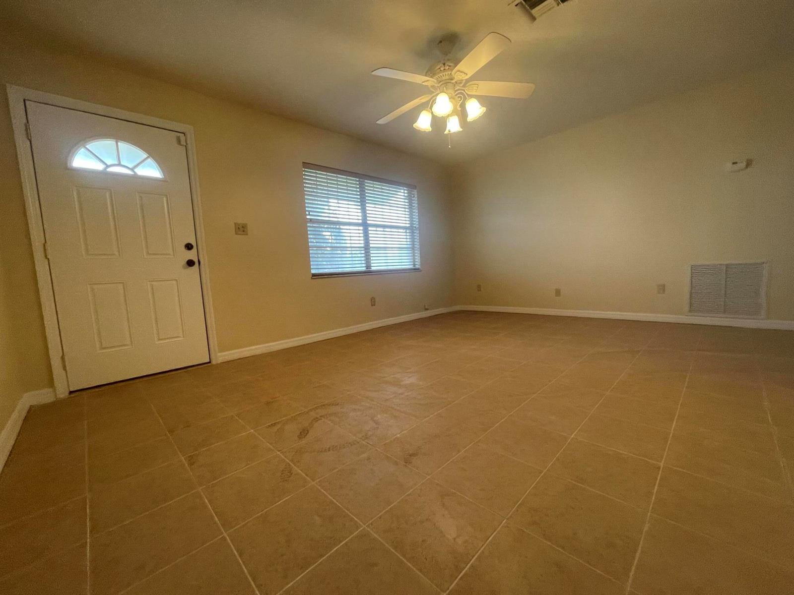 An empty room features beige tile flooring, a ceiling fan, and a white entry door — 3101 Avenue T, Fort Pierce FL 34947, FORT PIERCE, FL