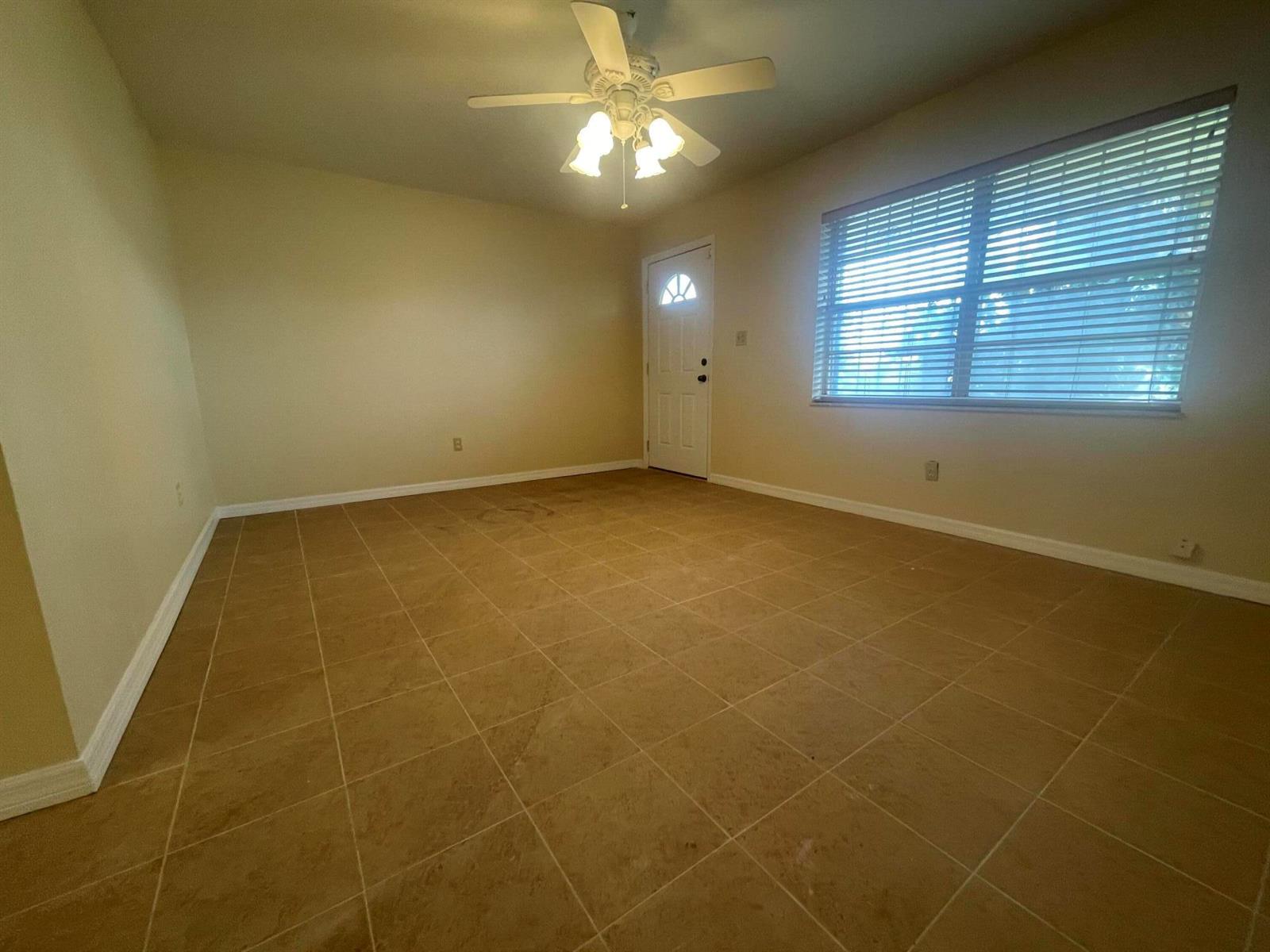 An empty room with tan tile flooring, a ceiling fan, and a window with blinds — 3101 Avenue T, Fort Pierce FL 34947, FORT PIERCE, FL