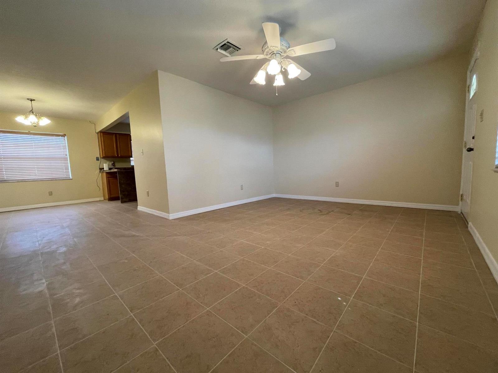 An open-concept living area features beige tile flooring, a ceiling fan, and a kitchen view — 3101 Avenue T, Fort Pierce FL 34947, FORT PIERCE, FL