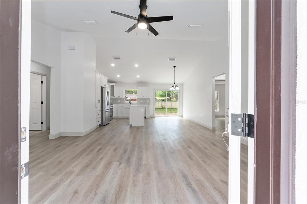 An open-concept kitchen and living area features white cabinetry, light wood flooring, and recessed lighting — 3368 SE 142ND, SUMMERFIELD, FL