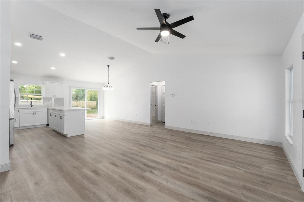 An open-concept living area features white walls, light wood-look flooring, and a modern kitchen — 3368 SE 142ND, SUMMERFIELD, FL