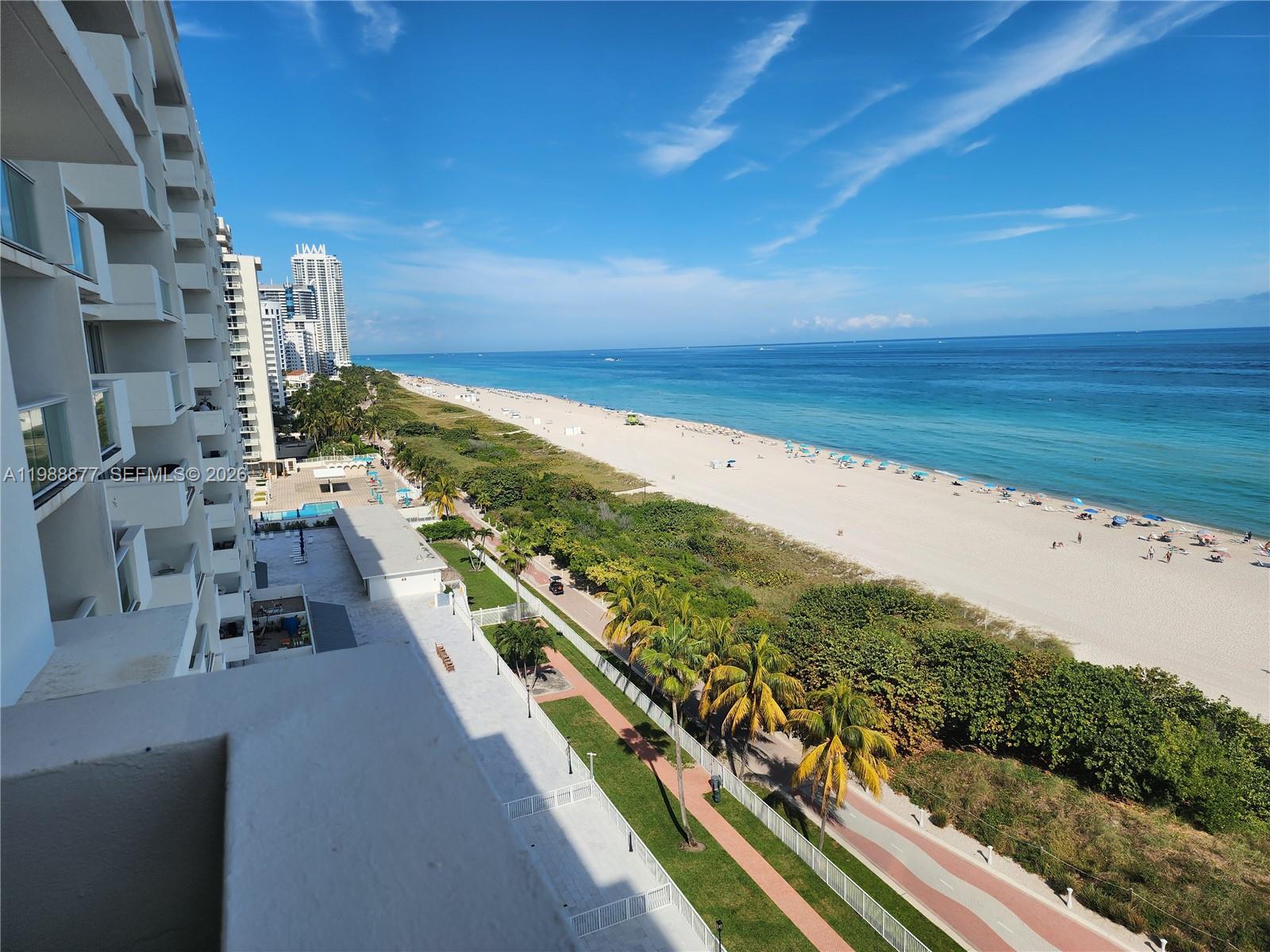 An elevated view shows a beach, ocean, and palm trees from a high-rise balcony — 5601 Collins Ave # 1110, Miami Beach FL 33140, MIAMI BEACH, FL