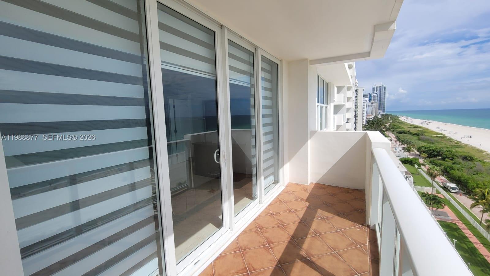 A balcony with tiled flooring overlooks a beach and ocean with high-rise buildings nearby — 5601 Collins Ave # 1110, Miami Beach FL 33140, MIAMI BEACH, FL
