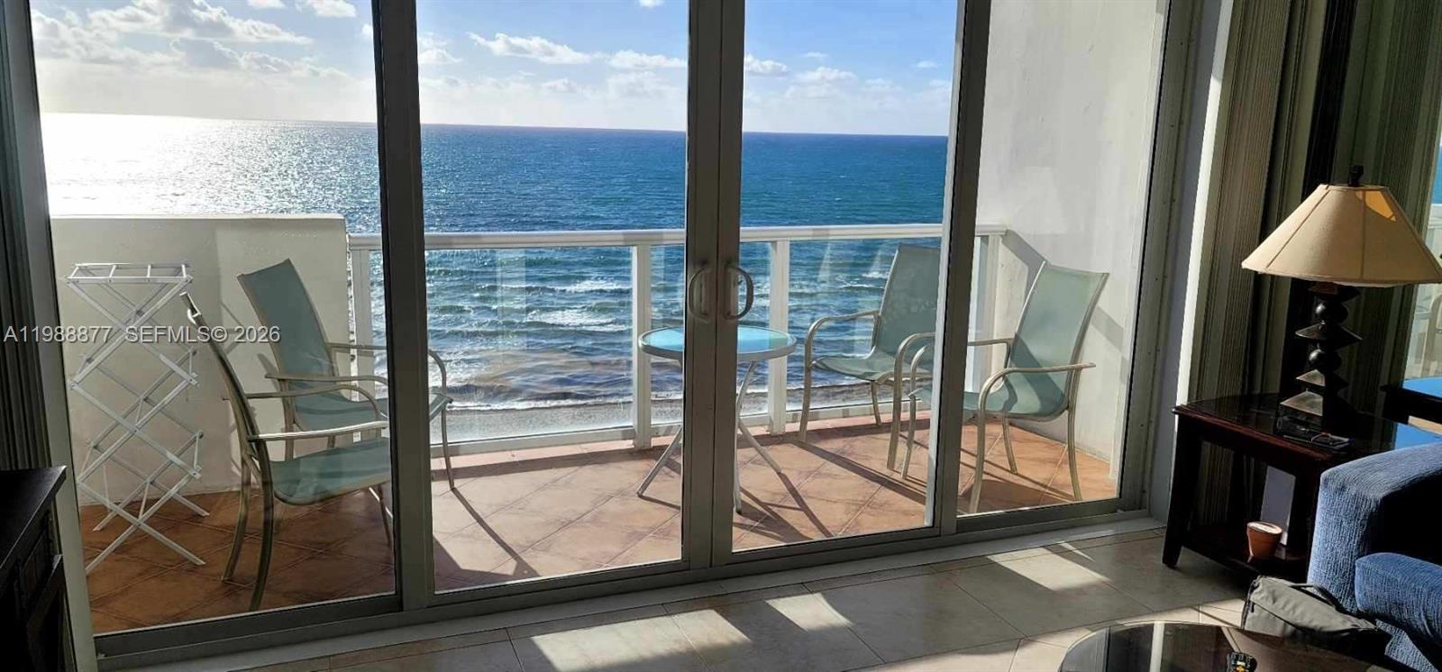 A balcony with chairs and a table overlooks the ocean through large sliding glass doors — 5601 Collins Ave # 1110, Miami Beach FL 33140, MIAMI BEACH, FL