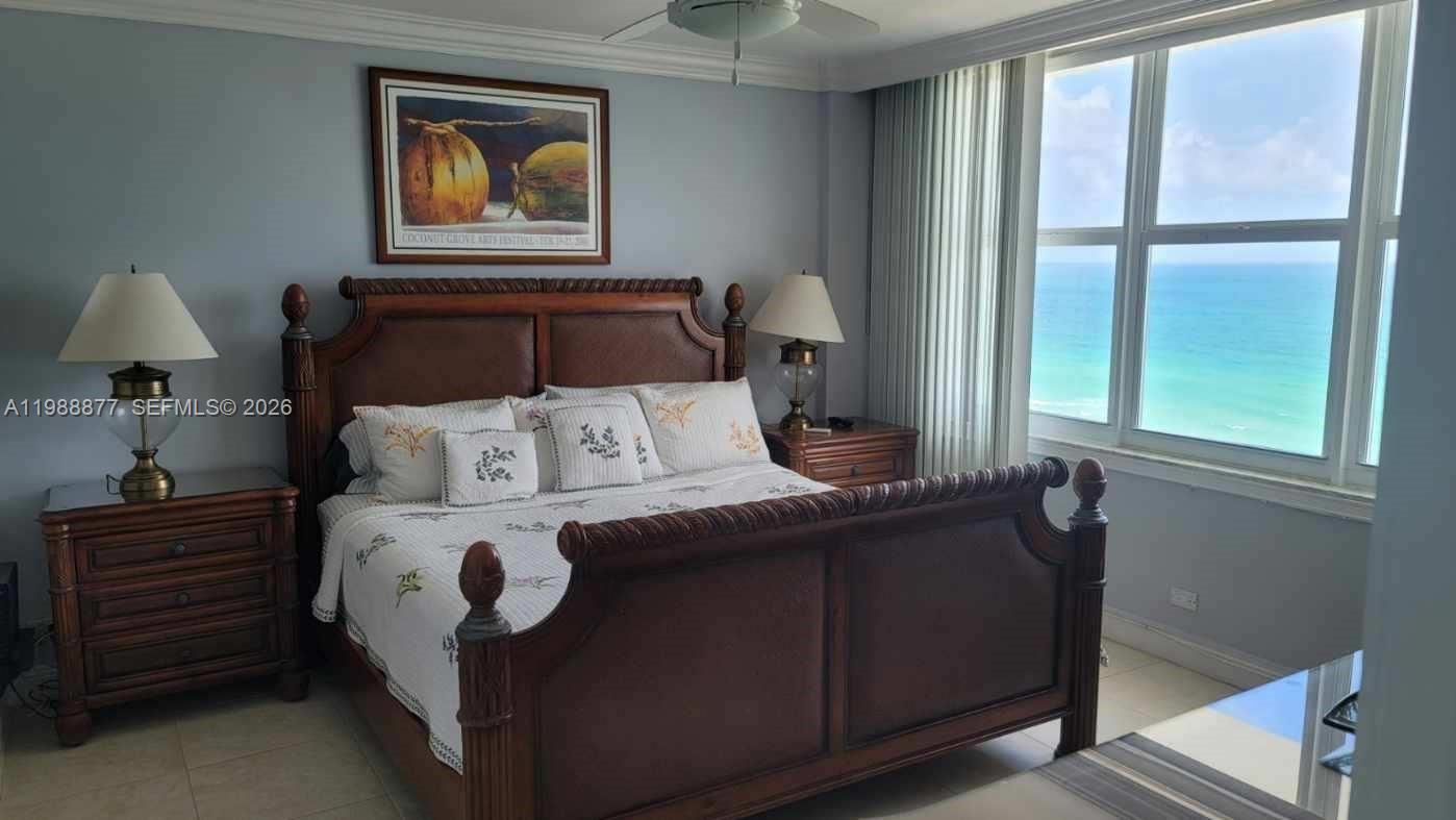 A bedroom features a wooden bed frame, two nightstands with lamps, and a large ocean-view window — 5601 Collins Ave # 1110, Miami Beach FL 33140, MIAMI BEACH, FL