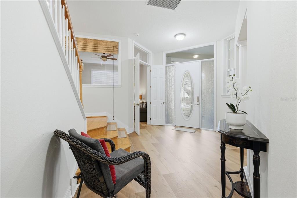 A bright entryway features light wood flooring, a white front door, and a staircase — 3409 54TH DR W UNIT H-103, BRADENTON, FL