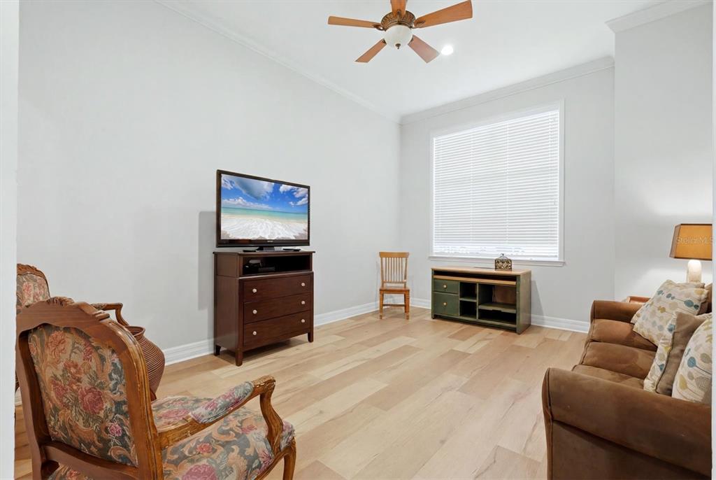 A living room features light wood flooring, a ceiling fan, and a large window — 3409 54TH DR W UNIT H-103, BRADENTON, FL
