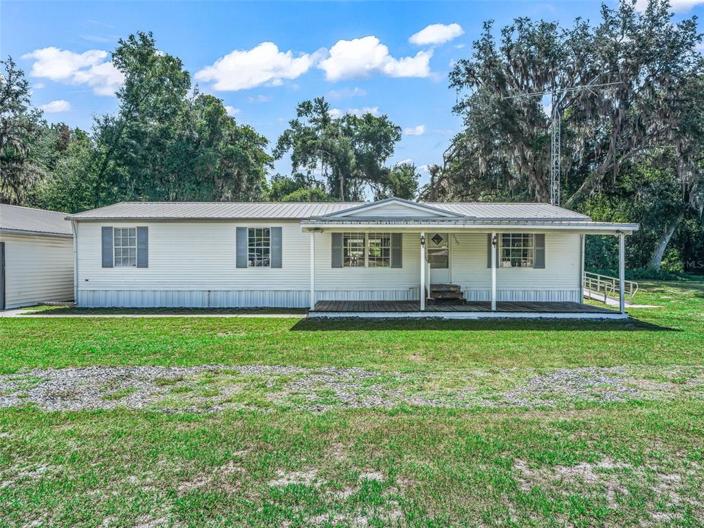 A single-story manufactured home with white siding, a metal roof, and a front porch — 7363 CR 763, BUSHNELL, FL
