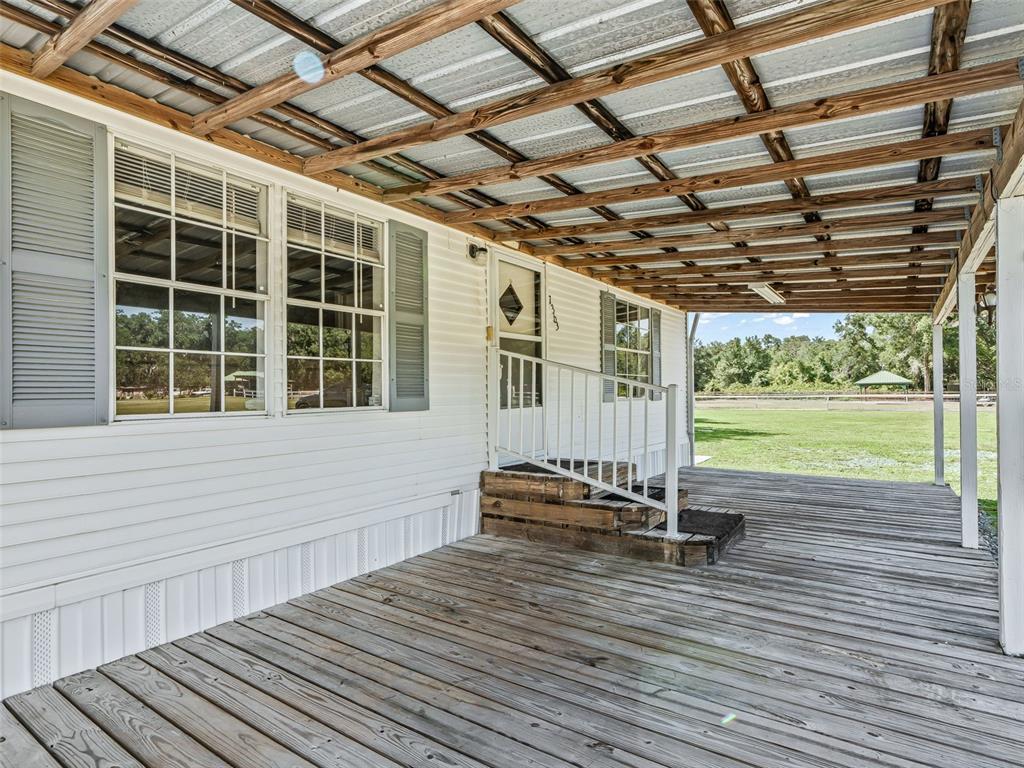 A wooden deck with a metal-roofed porch leads to the front entrance of a house — 7363 CR 763, BUSHNELL, FL