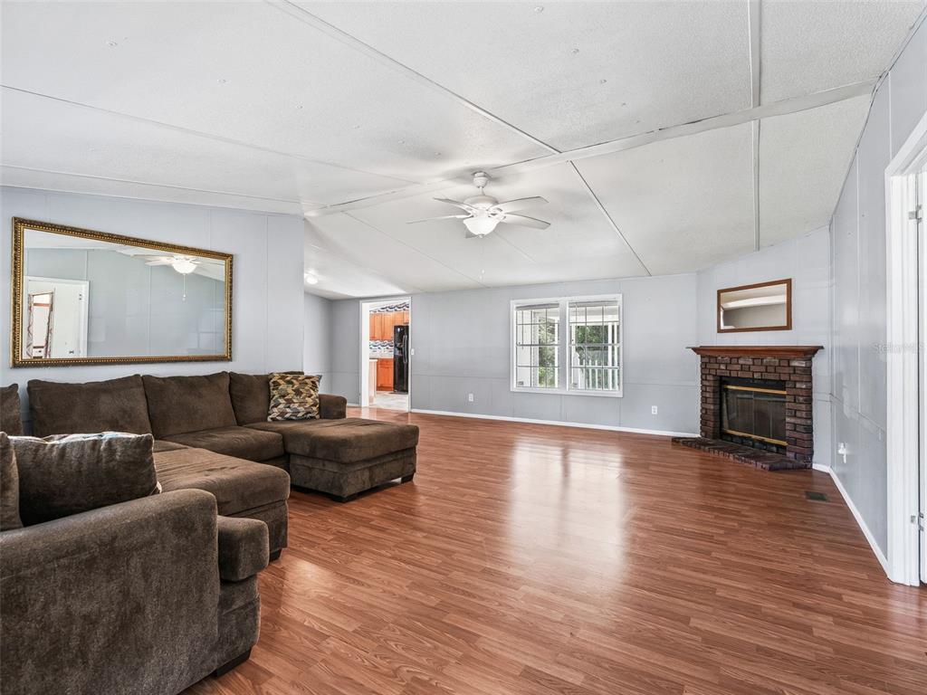 A living room features wood-look flooring, a brown sectional sofa, a fireplace, and a ceiling fan — 7363 CR 763, BUSHNELL, FL