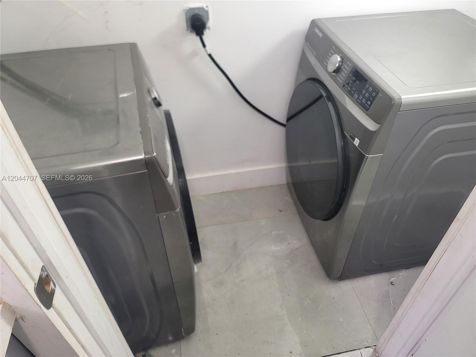 Two gray laundry appliances are positioned in a small room with a white wall — 512 NW 96th St # B, Miami FL 33150, MIAMI, FL