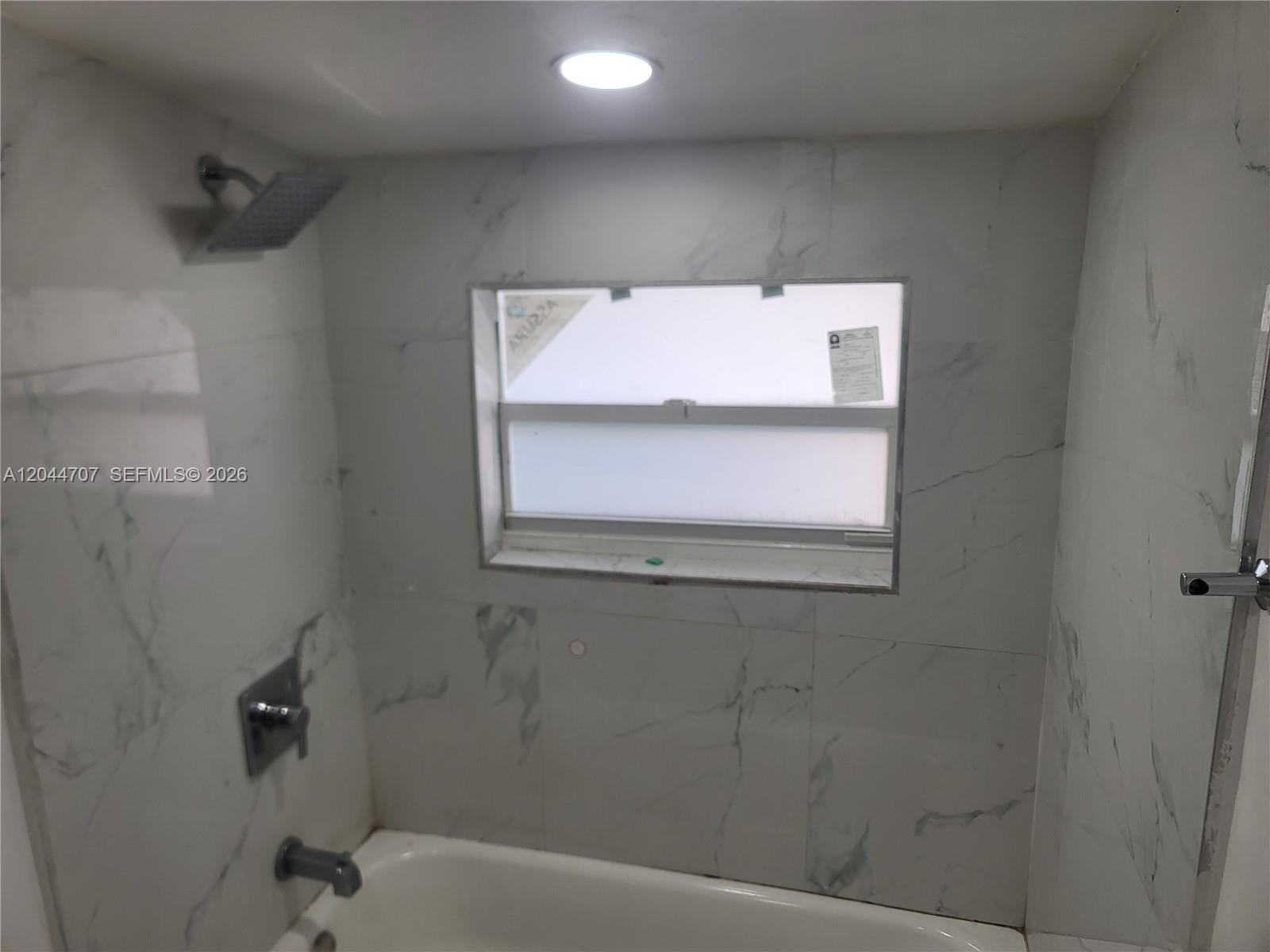 A bathroom shower area features white marble-look tiles, a bathtub, and a window — 512 NW 96th St # B, Miami FL 33150, MIAMI, FL