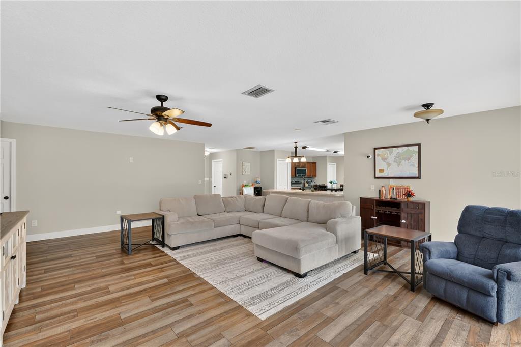 A living room with wood-look flooring, a sectional sofa, and an open kitchen in the background — 1985 MUSTANG COURT, ST CLOUD, FL
